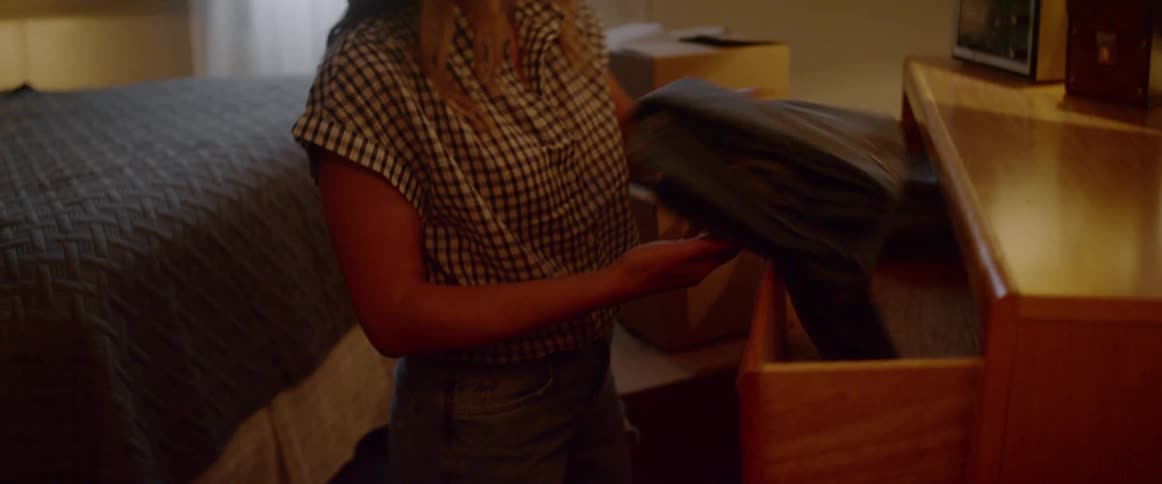 A woman removes pants from a dresser and places them in a cardboard box
