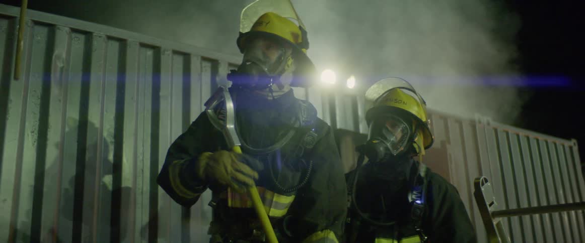 A fireman hand a tool to another fireman while aa third fireman is standing next to him