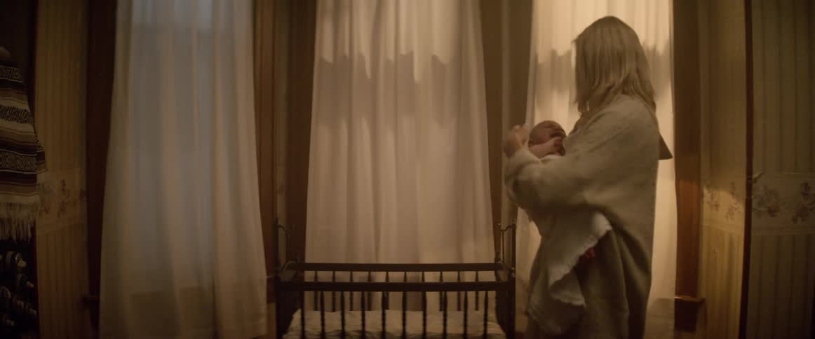 A woman standing next to a crib cradling and rocking a baby