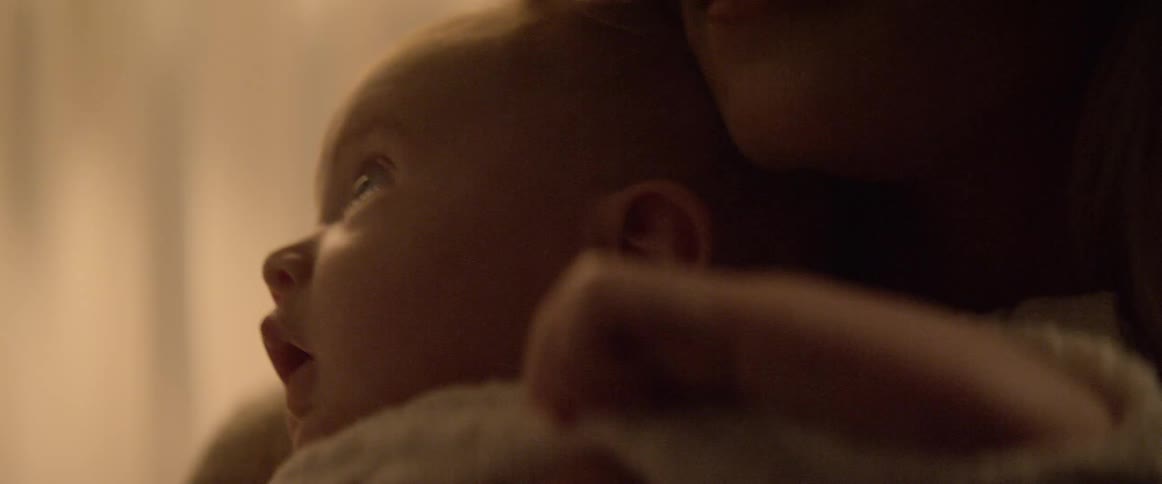 Woman rocks baby in her arms near curtained window