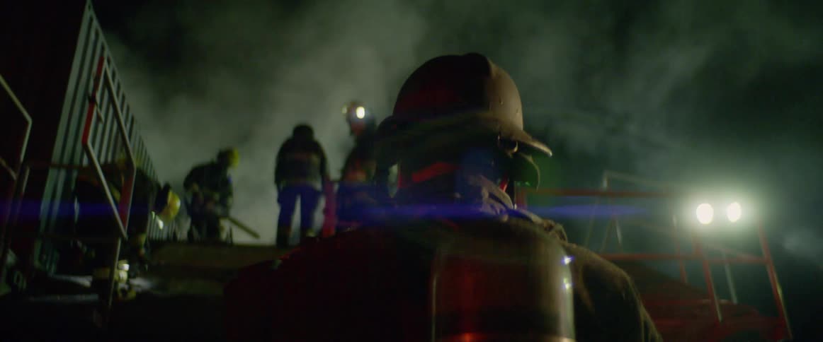Firefighters stand on the roof of a building with tools in hand