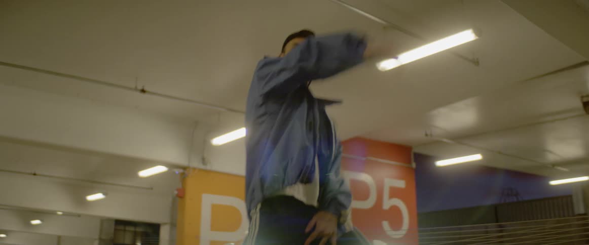 Dancer dances in parking garage in front of parked car with its headlights on