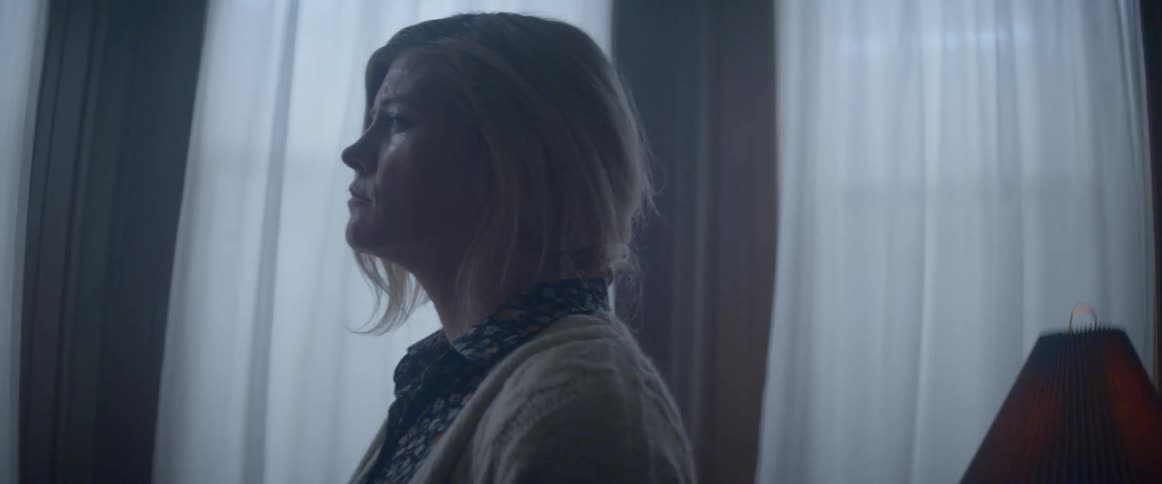 Woman wearing cardigan stands near window thinking