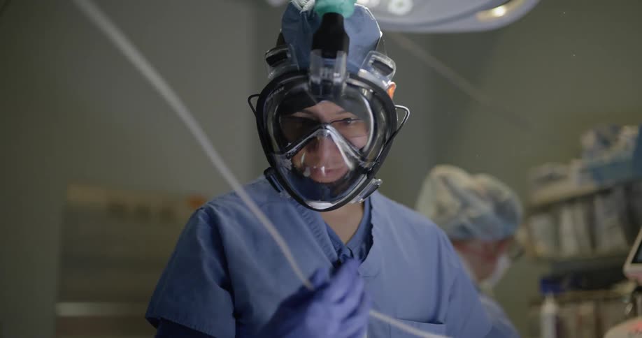 Doctor wearing full face mask and scrubs inspects tubing in operating room