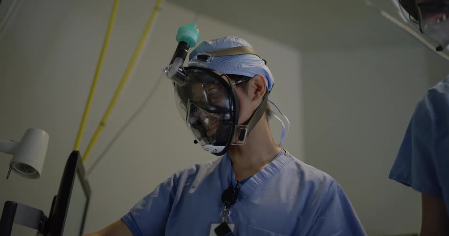 A doctor points to a screen while wearing a respiratory mask