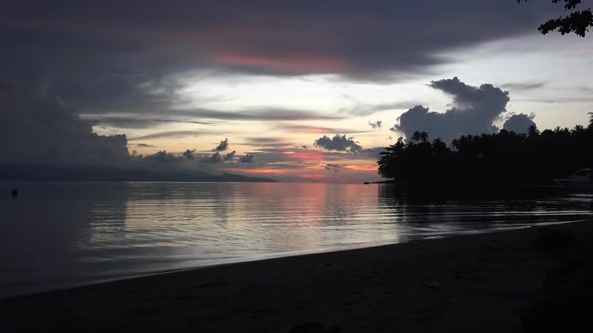 The sun sets behind water on a partly cloudy day