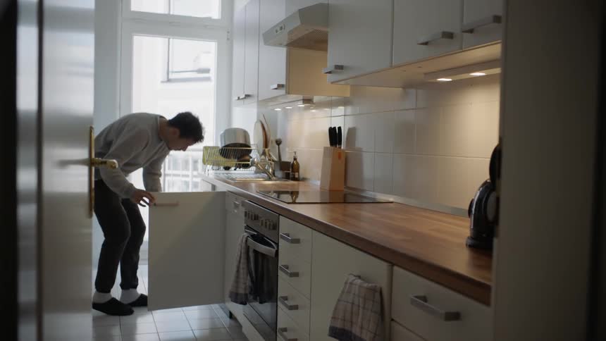 Man opens cupboard in kitchen and picks up cleaning implements