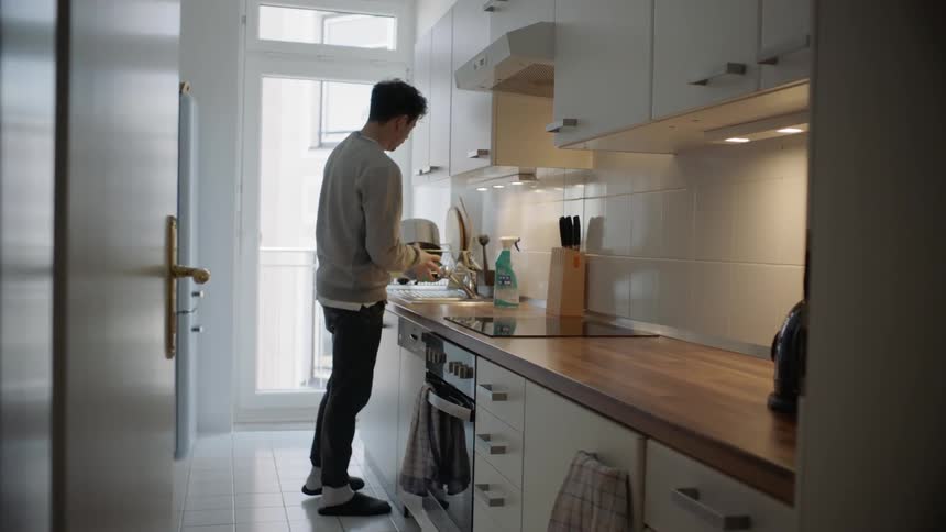 Man cleans dishes in kitchen sink