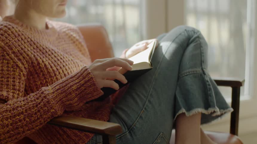 Woman sits curled up in chair reading a hardback book