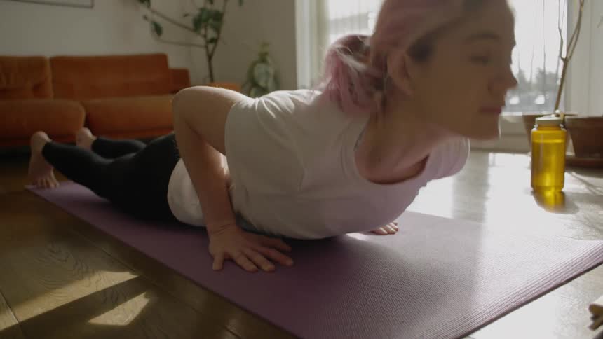 A pink haired woman performing stretches in her living room