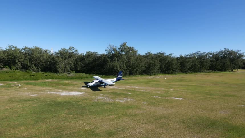 An aerial view of a small plane making a u-turn in a grassy field after having landed on a clear summer day