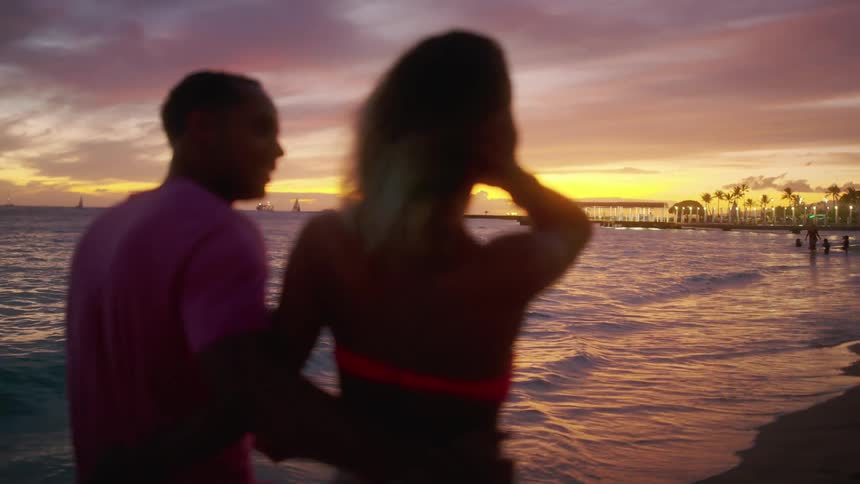 A man and woman walk along the beach at sunset
