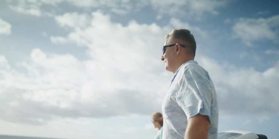 A man and woman get out of a car and hold hands and walk towards the water