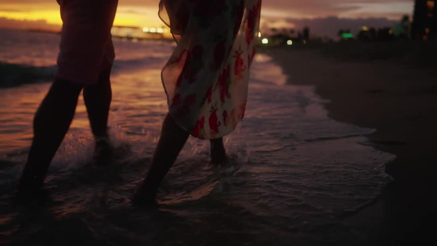 Couple walks hand in hand on beach at sunset