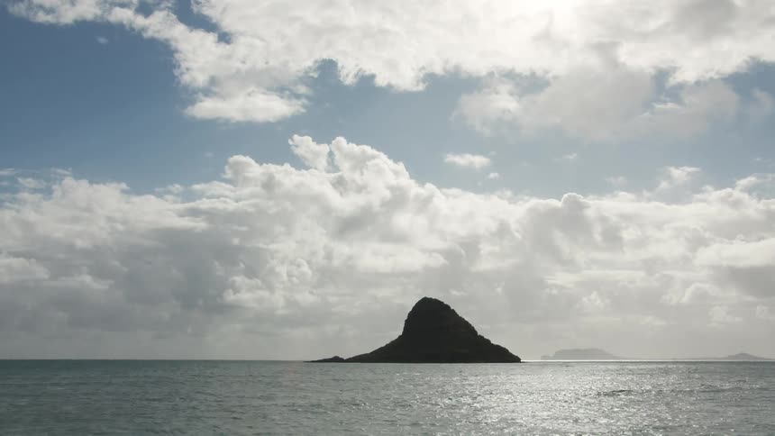 An island stands in the middle of the ocean under a cloudy sky