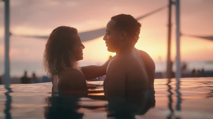 A man and a woman watch the sun from a pool