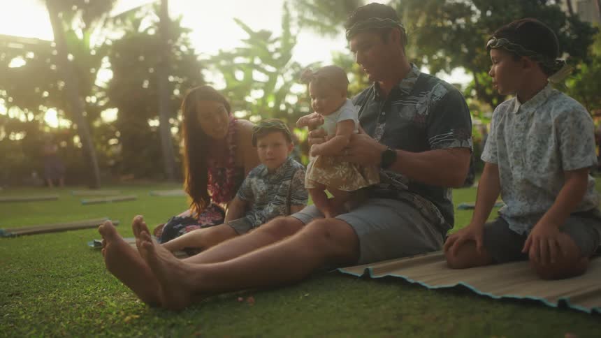 Family sits on grass playing together on vacation in hawaii