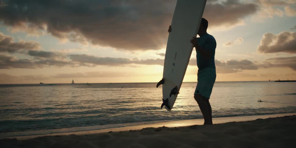 A man lifting a surfboard from the ground while standing on the beach