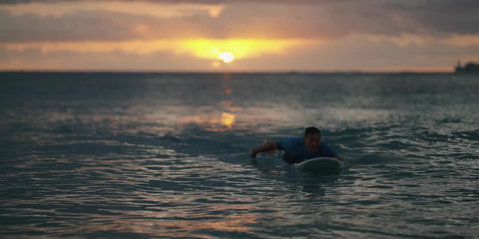 A surfer paddles toward the shore as the sun begins to rise