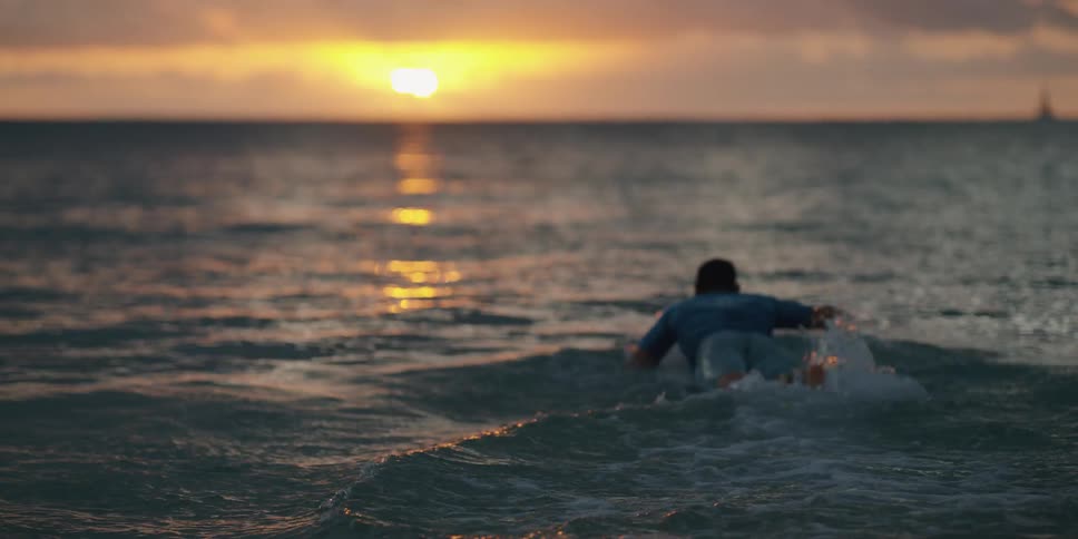 A man paddles his surfboard out in to the water