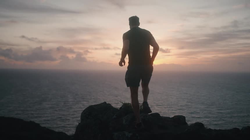 Man stands on cliff to watch sunset over the sea
