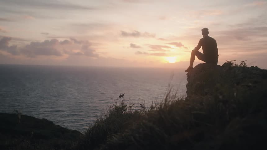A man is watching the sunset above the ocean