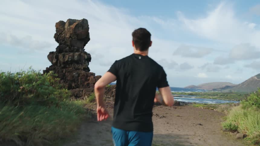 A man running along a rocky coastline on a sunny day