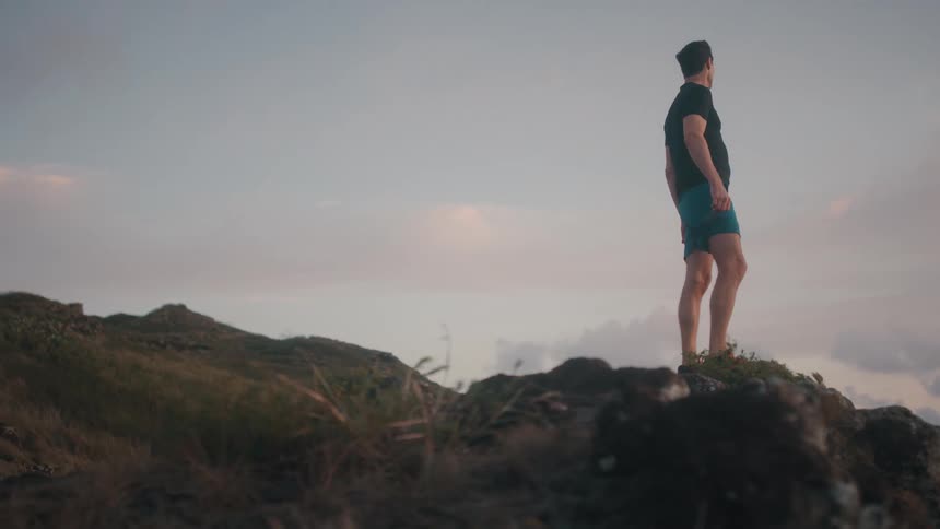 Man stands on hillock looking around under a cloudy sky