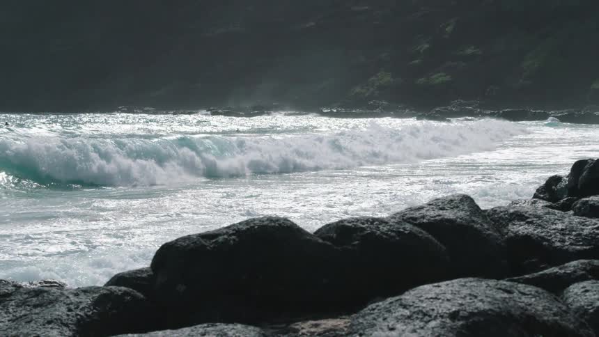 Ocean waves crashing into a rocky coast with people in the water