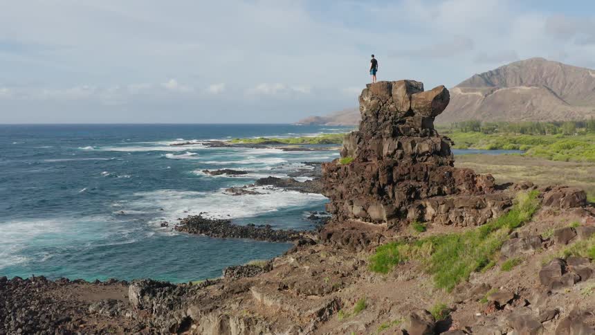 A male stands on top of a cliff overlooking the water below