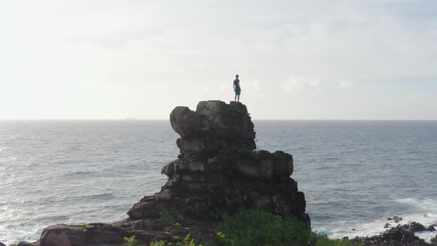 A man stands on top of a cliff and looks out over the water