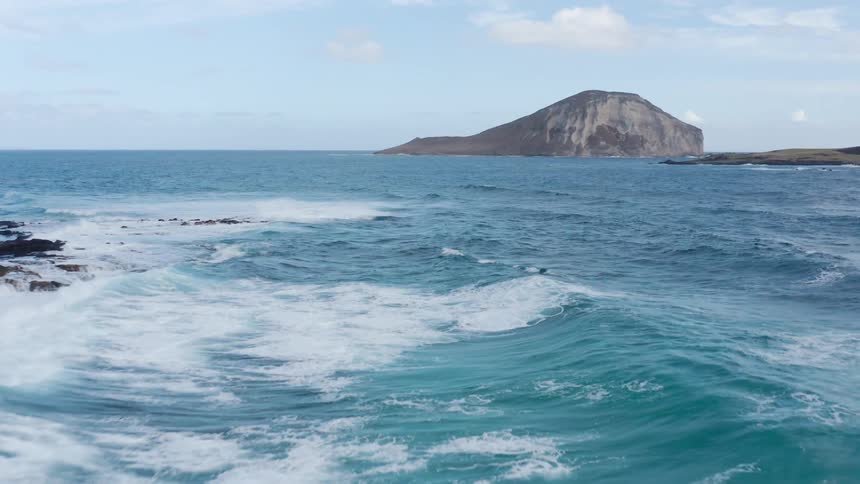 Waves race across blue ocean to crash against shore near stony island