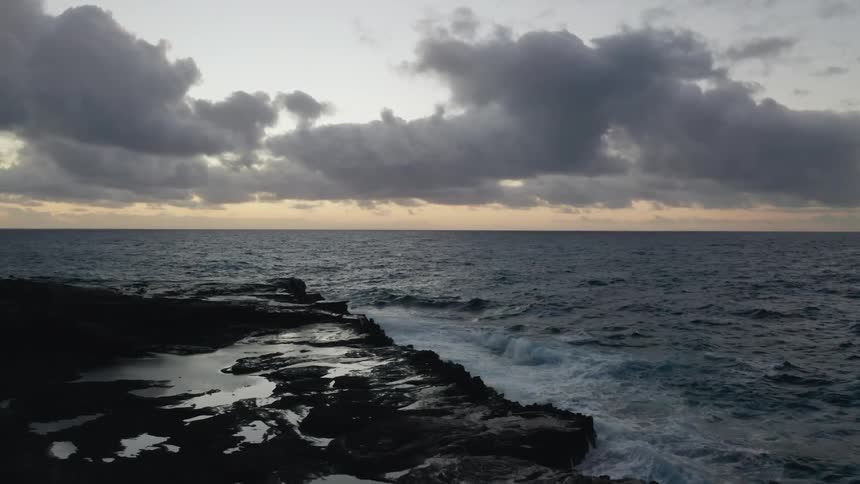 Waves crash into a rocky beach under a cloudy sky at dusk