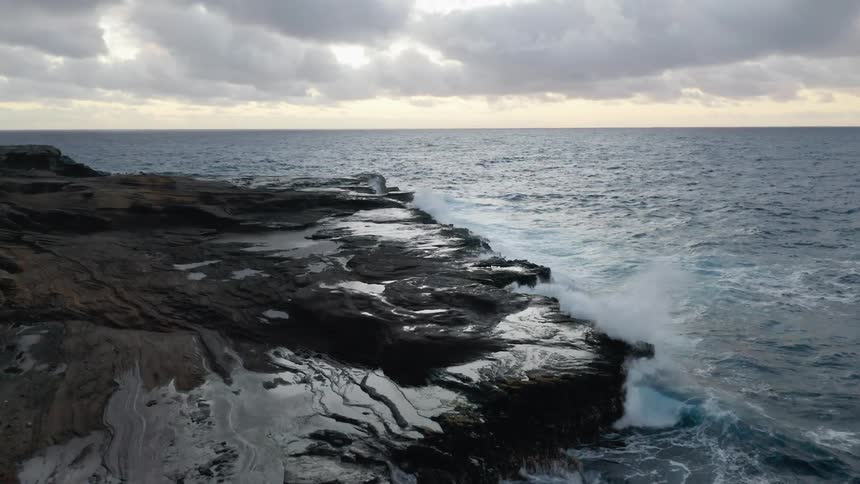 Ocean waves crash against the rocky shore on a cloudy day