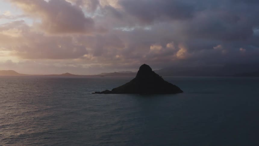 Small island sits in ocean with shore on the horizon