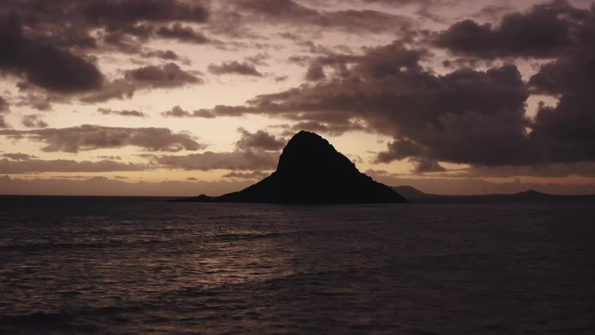 A lopsided cone shaped island on a cloudy evening