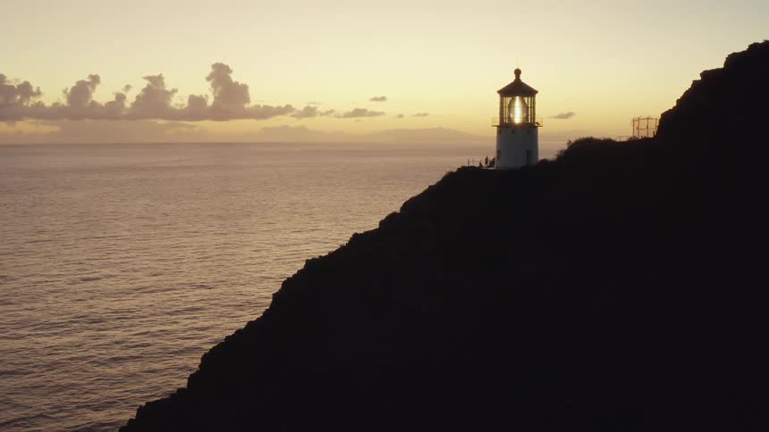 Lighthouse on cliff above ocean at sunset