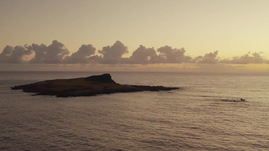 The sun sets along the ocean and an island