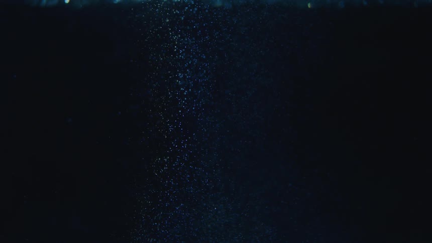 A column of glowing bubbles rises up in dark blue water
