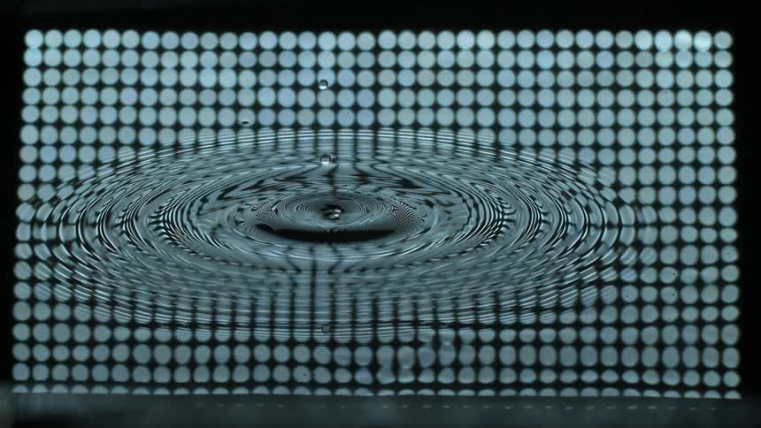 Slow motion water droplets causing ripple effect in front of polka dot background