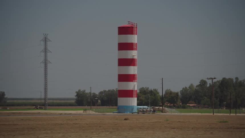 Vehicle travels down a country road near a striped water tower and farm land