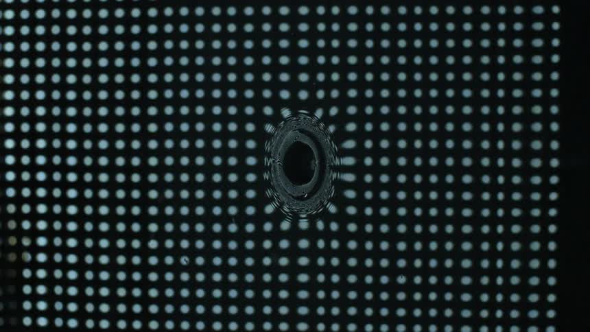 Water drop falls in slow motion and splashes into ripples above dotted grid