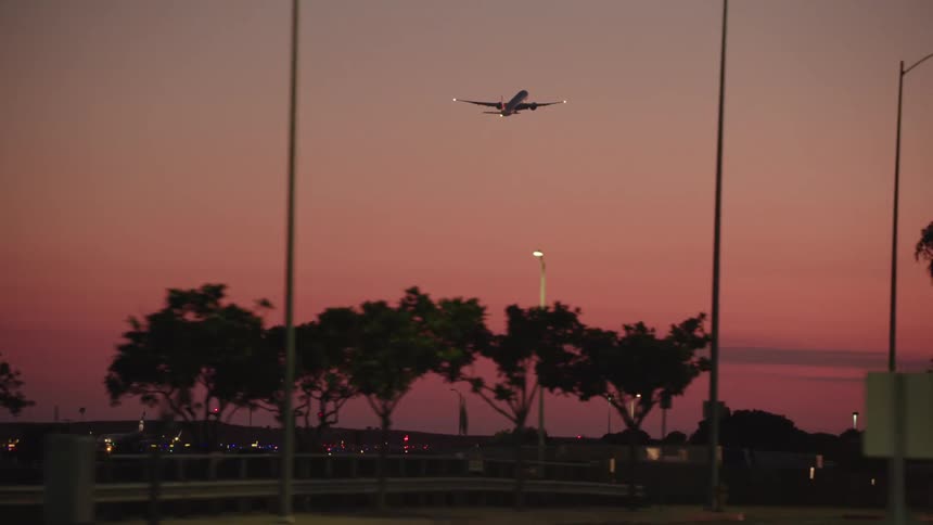 A view from the road far below of a plane taking off during a sunset