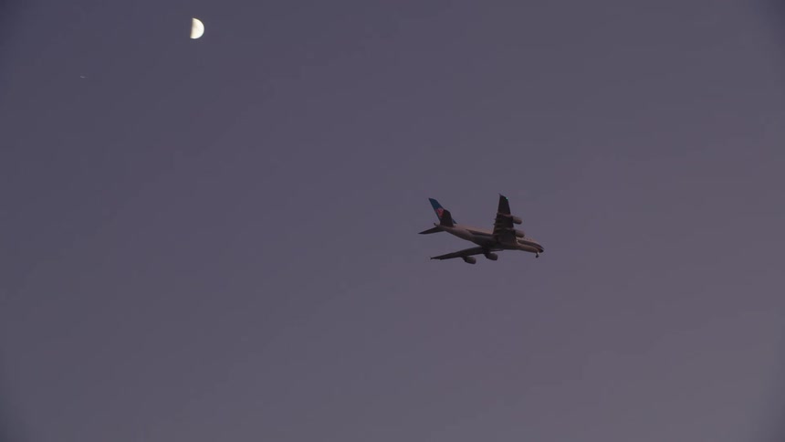 Commercial airliner flies in near moon at sunset