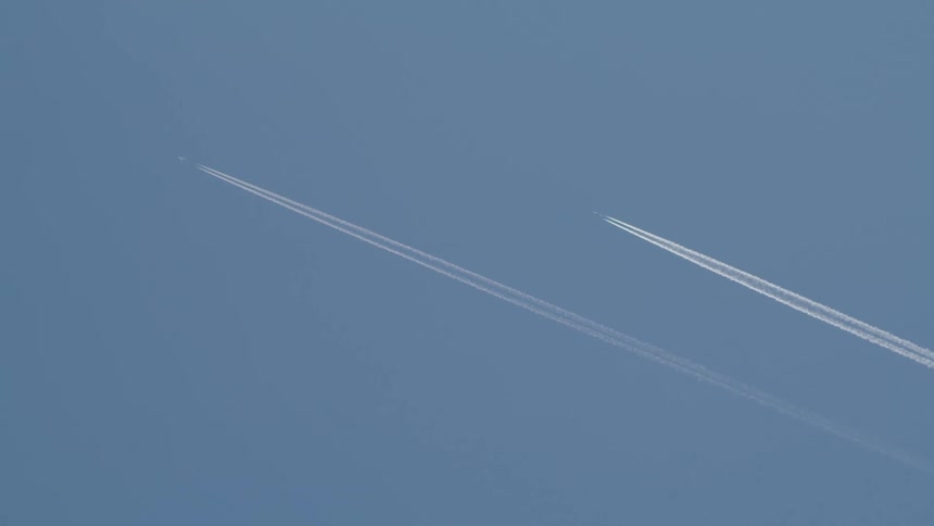 Two jets race across the sky above the tree tops leaving a contrail