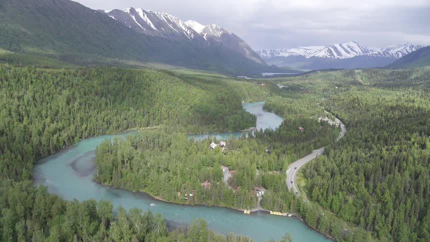 A river and road run through a forest that sits below a mountain range