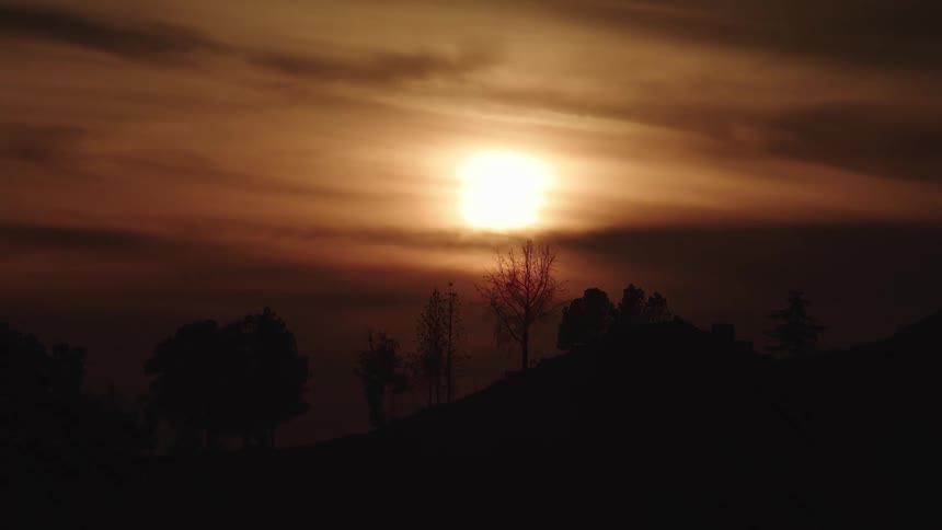 The sun sits on the horizon and silhouettes a hillside