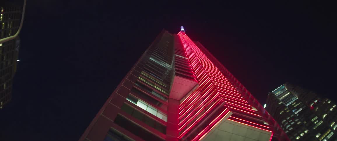 Red lights light up the side of a high rise building