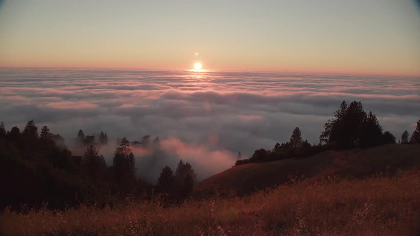 Hills leading to down to a sea of clouds illuminated by a low sun on the horizon