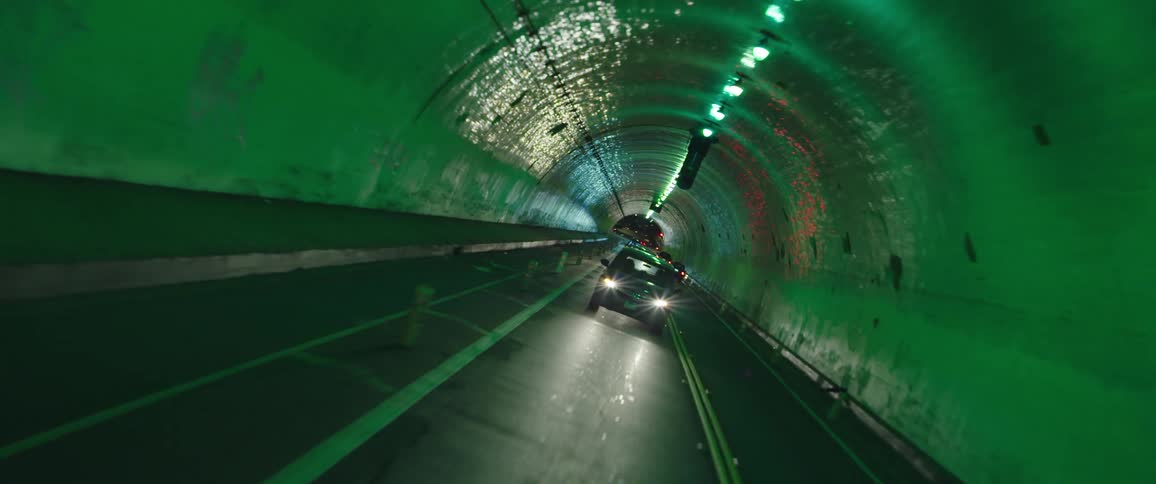 Cars driving through a long tunnel with well lit lights overhead
